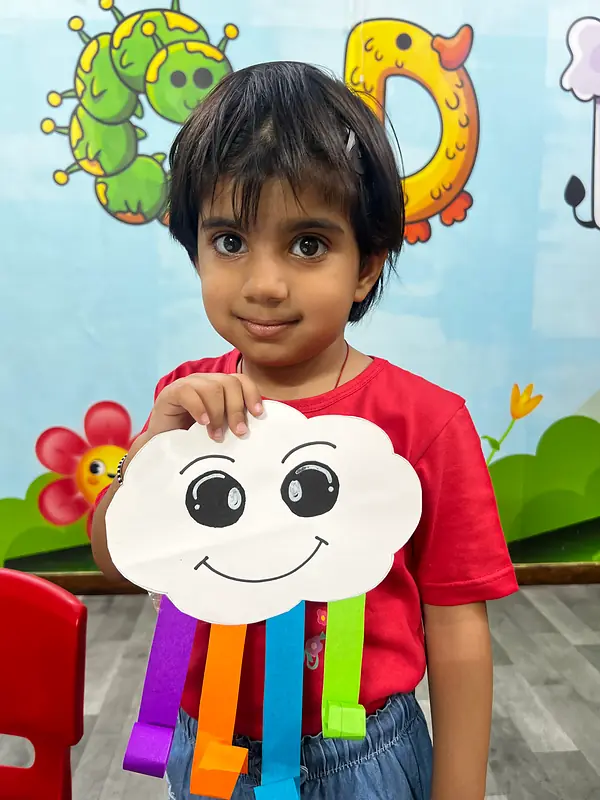 A boy holding up his rainbow cloud craft at summer camp