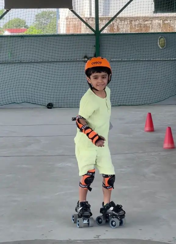 A boy in a helmet and pads smiles as he skates at summer camp