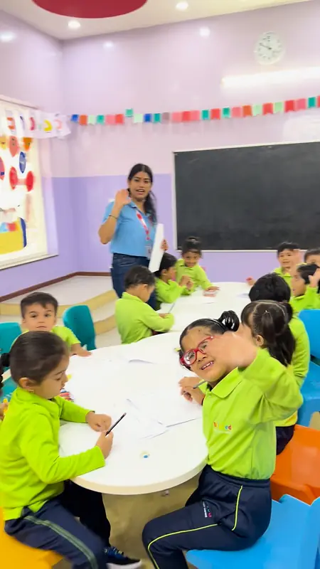 Children at their tables while the teacher talks from the front of the class