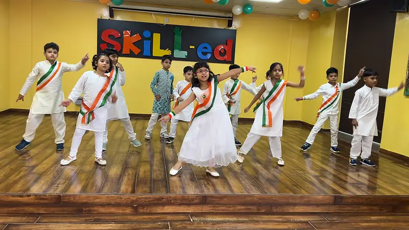 Students in white with tricolour sashes dance on stage