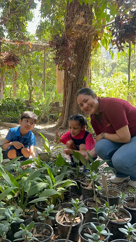A teacher shows two children how to water plants at the plant nursery