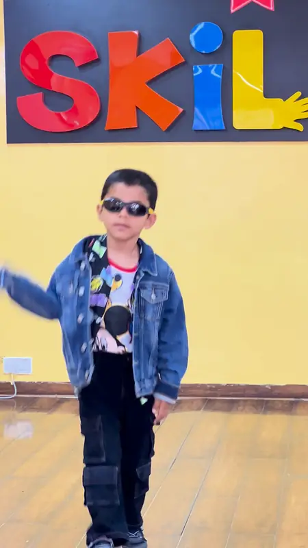 A boy in a denim jacket and sunglasses walks out in front of the Skill-ed letters