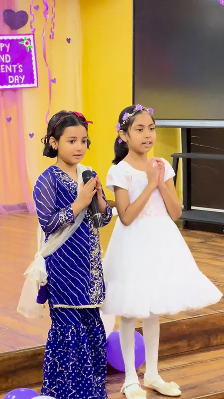 Two student anchors greet the grandparents with folded hands